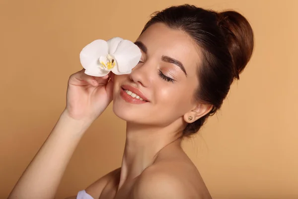 Close-up portret van jong mooi meisje met vlekkeloze huid houdt Witte orchidee bloem in haar hand. Huidverzorging, Beauty en cosmetica concept. — Stockfoto