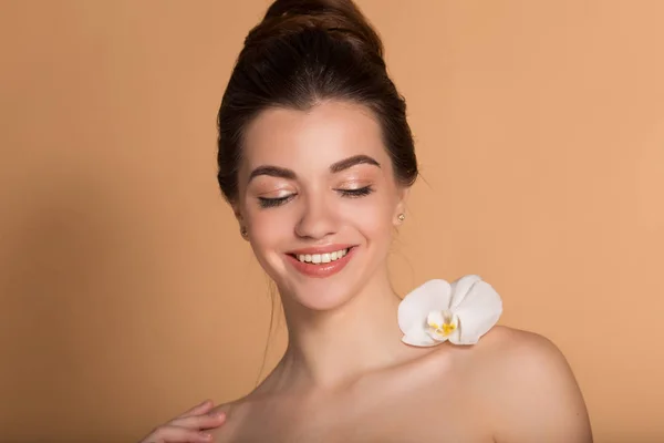 Retrato de cerca de una joven hermosa niña con una piel impecable con una flor de orquídea blanca en el hombro. Cuidado de la piel, belleza y cosméticos concepto . — Foto de Stock