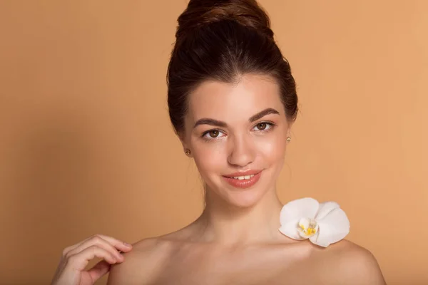 Closeup portrait of young beautiful girl with flawless skin with white orchid flower on her shoulder. Skin care, beauty and cosmetics concept. — Stock Photo, Image