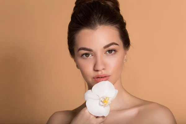 Νεαρό όμορφο κορίτσι με άψογο δέρμα κρατά λευκό λουλούδι ορχιδέα στα χέρια της. Ιδέα φροντίδας δέρματος, ομορφιάς και καλλυντικών. — Φωτογραφία Αρχείου