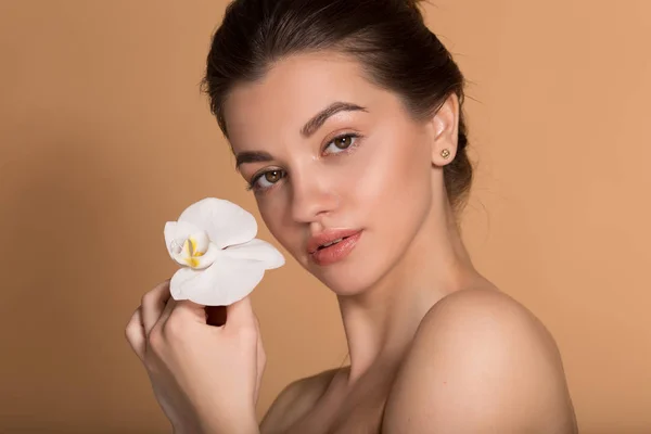 Νεαρό όμορφο κορίτσι με άψογο δέρμα κρατά λευκό λουλούδι ορχιδέα στα χέρια της. Ιδέα φροντίδας δέρματος, ομορφιάς και καλλυντικών. — Φωτογραφία Αρχείου