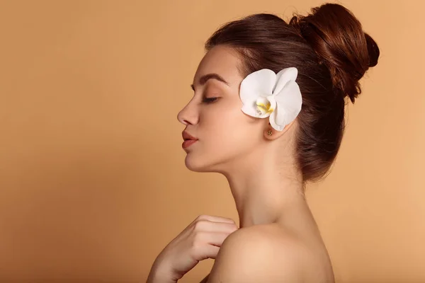 Joven hermosa chica con la piel impecable está sosteniendo flor de orquídea blanca en sus manos. Cuidado de la piel, belleza y cosméticos concepto . — Foto de Stock