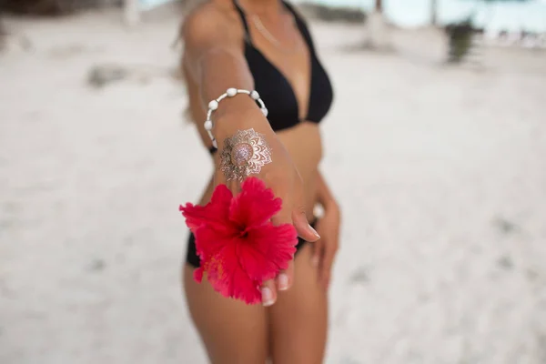 Jovem bronzeada com corpo perfeito com tatuagem na mão e flor vermelha relaxando na praia. Conceito de beleza e moda . — Fotografia de Stock