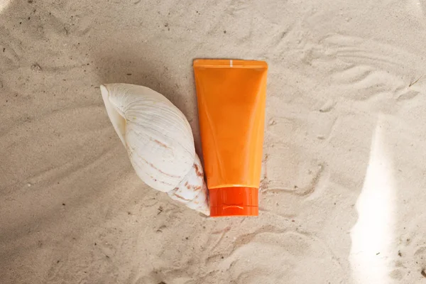 Jar of sunscreen and shell on the sand. Skin protection concept.