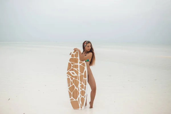 ザンジバルの干潮時に曇った夏の日にビーチでサーフボードでスポーツをしているスポーティな日焼けした体を持つ若いセクシーな女性 — ストック写真
