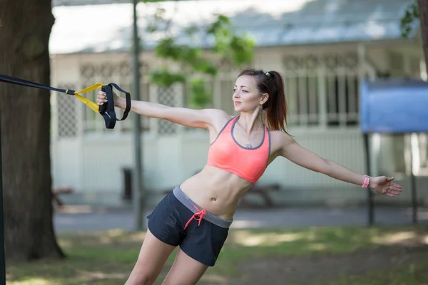 Красивая молодая женщина делает упражнения на открытом воздухе с TRX. Здоровый образ жизни, тренировки на trx. Общие упражнения по сопротивлению телу . — стоковое фото