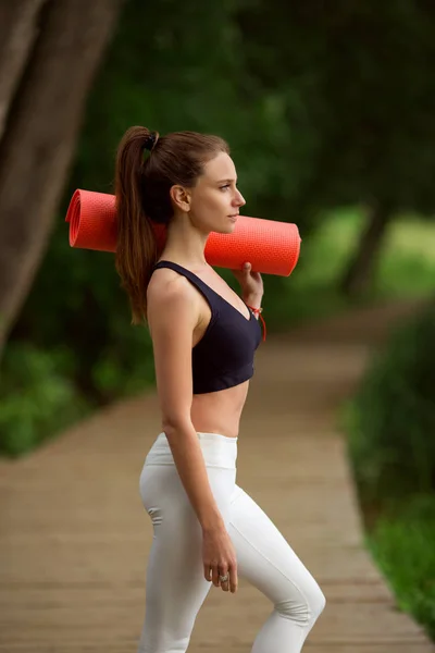 Menina muito esportiva com tapete de ioga ao ar livre no parque verde, hora de verão — Fotografia de Stock