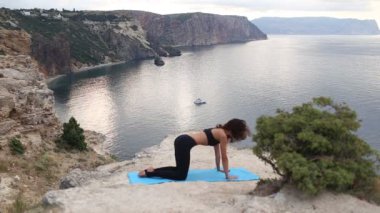 Dağ lık uçurumda yoga yapan güzel bir kadın. Deniz manzaralı gün doğumunda spor.