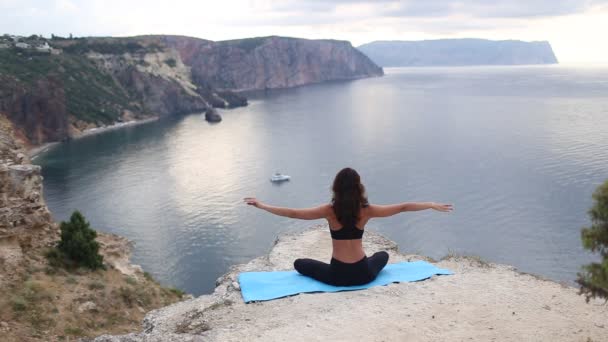 Mulher bonita fazendo meditação de ioga no penhasco da montanha. Desporto ao nascer do sol com vista mar . — Vídeo de Stock