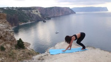 Deniz manzaralı dağ uçurumunda esneme ve denge egzersizleri yapan güzel kadın. Gün doğumunda spor.