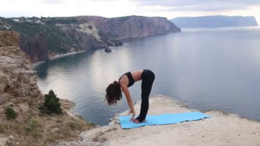 Deniz manzaralı dağ uçurumunda esneme ve denge egzersizleri yapan güzel kadın. Gün doğumunda spor.