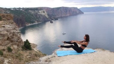 Deniz manzaralı dağ uçurumunda esneme ve denge egzersizleri yapan güzel kadın. Gün doğumunda spor.