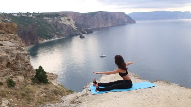 Hermosa mujer haciendo estiramiento en el acantilado de la montaña con vista al mar. Deporte al amanecer . — Vídeo de stock