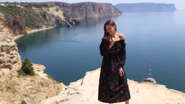 Młoda piękna kobieta w długiej sukni na górskim klifie oglądając na błękitne morze — Wideo stockowe