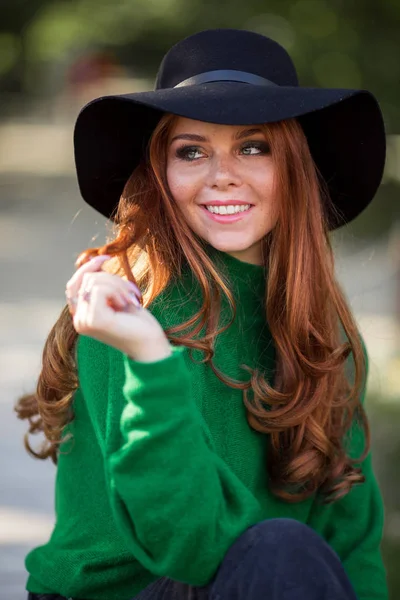 Sunshine joven sonriente mujer con el pelo rizado rojo está usando suéter verde y sombrero en el parque de otoño . —  Fotos de Stock