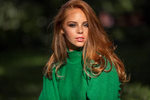 Sunshine young smiling woman with red curly hair is wearing green sweater in autumn park. — Stock Photo, Image