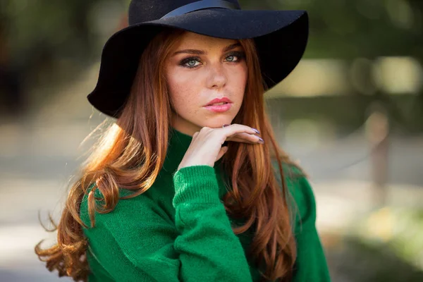 Sunshine jeune femme souriante aux cheveux bouclés rouges porte un pull vert et un chapeau dans le parc d'automne . — Photo