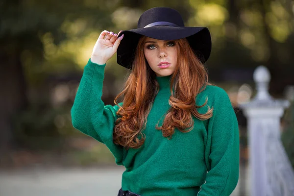Sunshine young teen girl with red curly hair is wearing green knitted sweater and hat in autumn park. — Stock Photo, Image