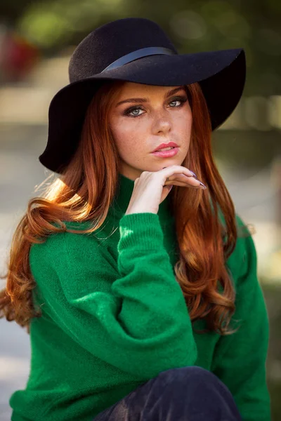 Portrait of sunshine young teen girl with red curly hair is wearing green sweater and fashion hat in autumn park. — Stock Photo, Image