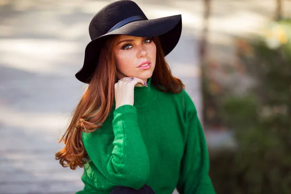 Portrait de soleil jeune adolescente aux cheveux bouclés rouges porte un pull vert et un chapeau de mode dans le parc d'automne . — Photo