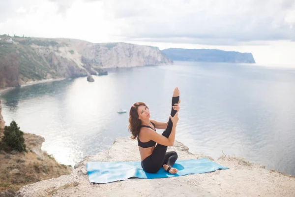 Bella donna magra pratica yoga e pilates sulla scogliera della montagna con la vista sul mare. Concetto di stile di vita sportivo e heathy . — Foto Stock