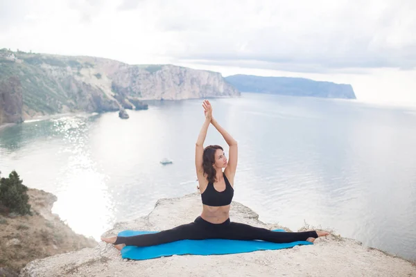 Bella donna magra pratica yoga e pilates sulla scogliera della montagna con la vista sul mare. Concetto di stile di vita sportivo e heathy . — Foto Stock