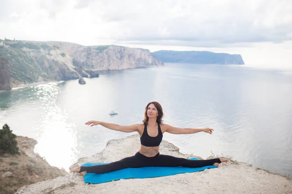 Vacker smal kvinna praxis yoga och Pilates på klippan av berget med havsutsikt. Sportiv och heathy livsstil Concept. — Stockfoto