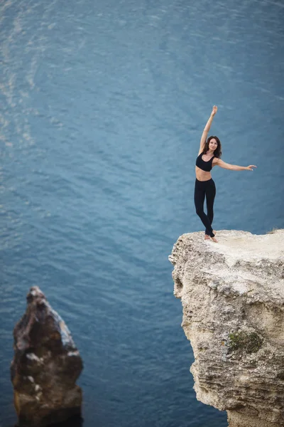 Beautiful slim woman practices yoga and pilates on the cliff of mountain with the sea view. Sportive and heathy lifestyle concept. — Stock Photo, Image