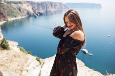 Mükemmel makyaj ile genç güzel kadın mavi deniz manzaralı dağ kenarında moda elbise giyiyor