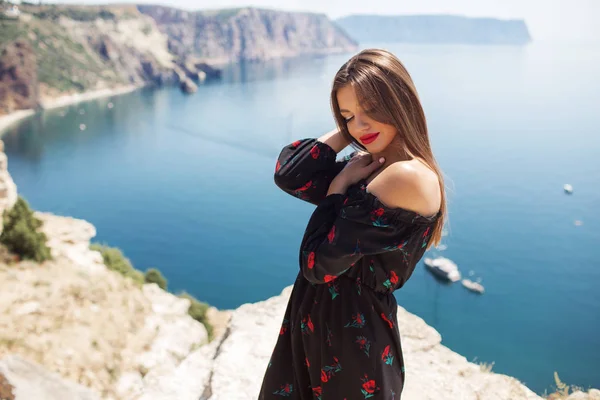 Ung vacker kvinna med perfekt makeup bär mode klänning på klippan av berget med blå havsutsikt — Stockfoto