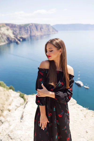 Mulher bonita nova com maquiagem perfeita está vestindo vestido de moda no penhasco da montanha com a vista azul do mar, conceito de viagem — Fotografia de Stock