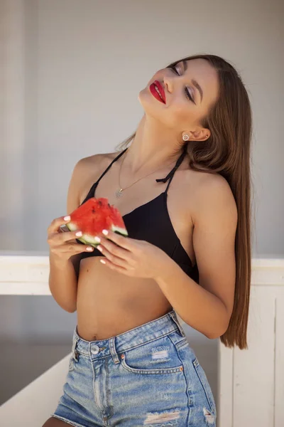 Fashion portrait of a sexy girl with perfect makeup is eating watermelon on the beach — Stock Photo, Image