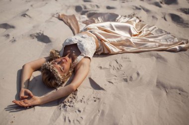 Güzel gelin Dubai'de büyük çölde kum üzerinde yatan moda uçan elbise ve çelenk giyiyor.