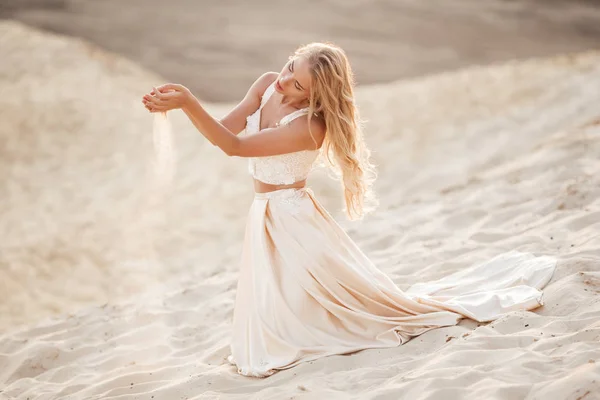 Retrato de novia hermosa está usando vestido de vuelo de moda sentado en la arena en el gran desierto de Dubai . — Foto de Stock