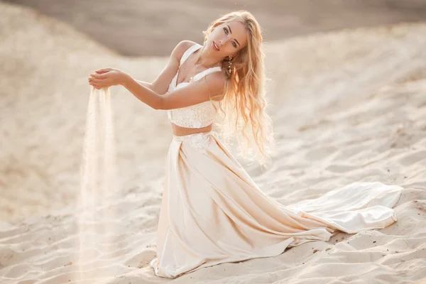 Porträtt av vackra bruden bär mode flygande klänning sitter på sand i den stora öknen i Dubai. — Stockfoto