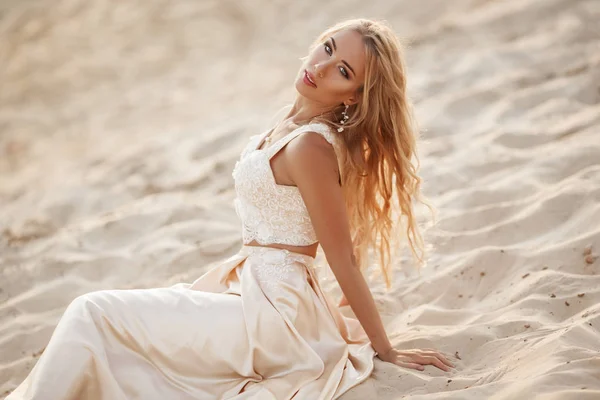 Portrait of beautiful bride is wearing fashion flying dress sitting on sand in the great desert in Dubai. — Stock Photo, Image