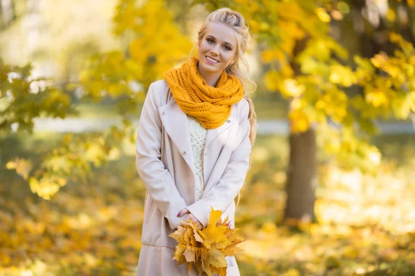 예쁜 금발의 십대 소녀가 노란 잎으로 가을 공원에서 걷고있습니다. — 스톡 사진