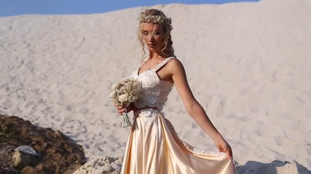 美しい花嫁は、ドバイの大きな砂漠でファッションフライングドレスとリースを着ています. — ストック動画
