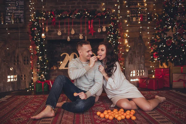 Casal encantador no interior de Natal no estúdio estão comendo mandarinas . — Fotografia de Stock