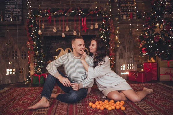 Casal encantador no interior de Natal no estúdio estão comendo mandarinas . — Fotografia de Stock