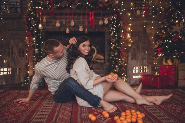 Preciosa pareja mujer y hombre están acostados en casa con mandarinas. Tiempo de Navidad . — Foto de Stock