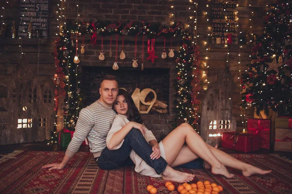 Lovely couple woman and man are lying at home near fireplace with mandarins. Xmas time. — Stock Photo, Image