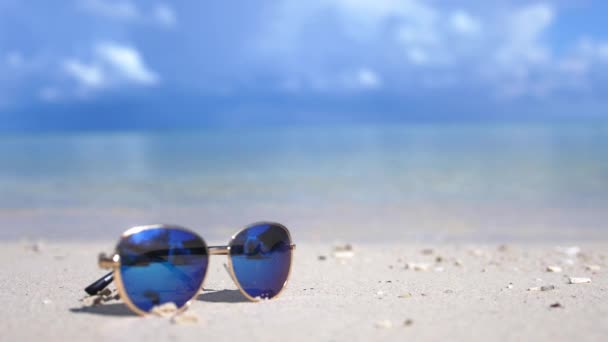 Cestování a dovolená koncept. Modré brýle na pláži Bílého moře. Lazure tyrkysové moře v pozadí s kopie prostoru. slwo pohyb. 3840 x 2160