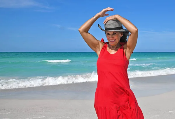 Kumsalda Kırmızı Bir Yaz Elbisesi Giyen Şapkasını Rüzgarda Tutan Güzel Stok Resim
