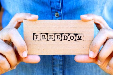 Özgürlük Siyah alfabe pullar tarafından yapılan kelime ile karton kartı tutan kadın el. Denim arka planlar. 