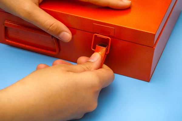 Mujer manos cerradura de apertura en caja de metal naranja en mesa azul . — Foto de Stock