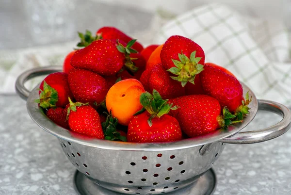 Fresas y albaricoques en un colador sobre la mesa . — Foto de Stock