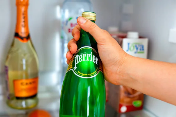 Frau holt Flasche mit Perrier-Wasser aus Kühlschrank. — Stockfoto