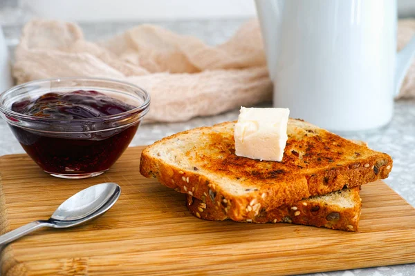 Deux toasts avec un morceau de beurre sur une planche en bois et un bol avec j — Photo