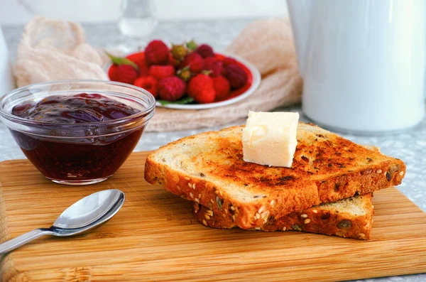 Deux toasts avec un morceau de beurre sur une planche en bois et un bol avec ra — Photo